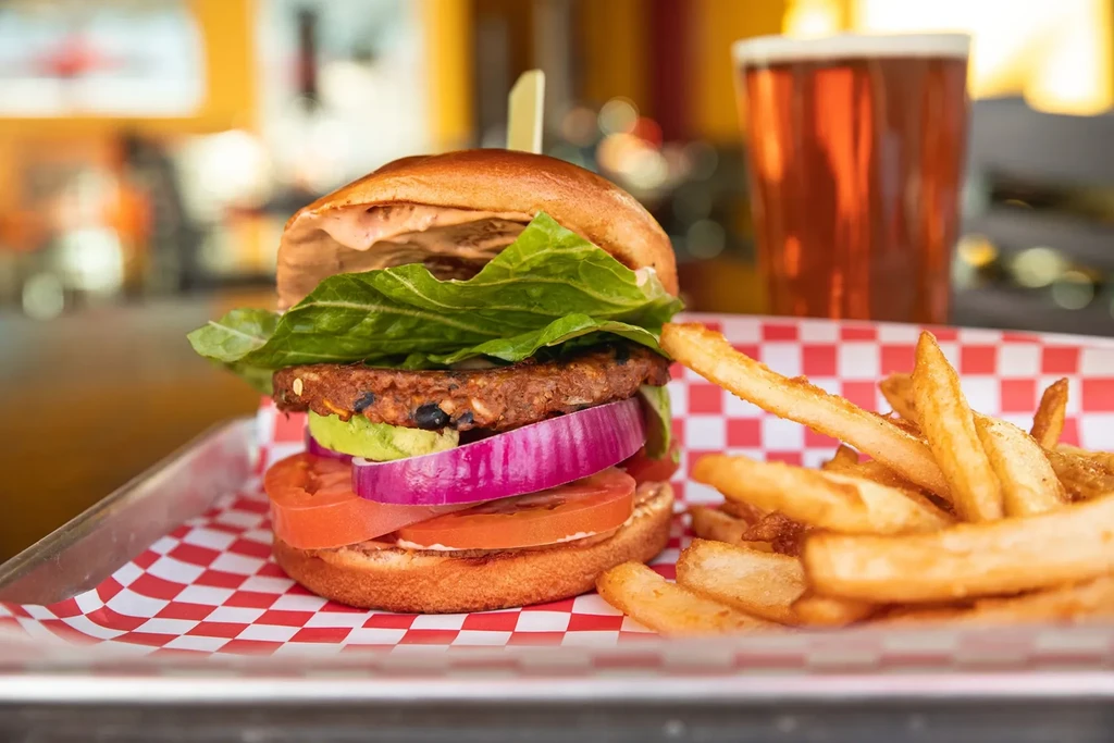 Black bean burger with avocado and fries on a checkered tray.