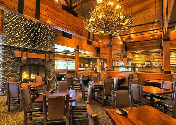 Rustic lodge dining room with stone fireplace and antler chandelier.
