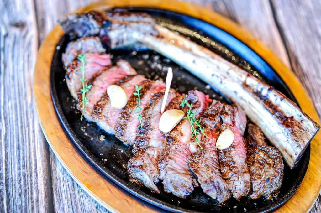 Sliced medium-rare Tomahawk steak with garlic and thyme on sizzling cast iron.