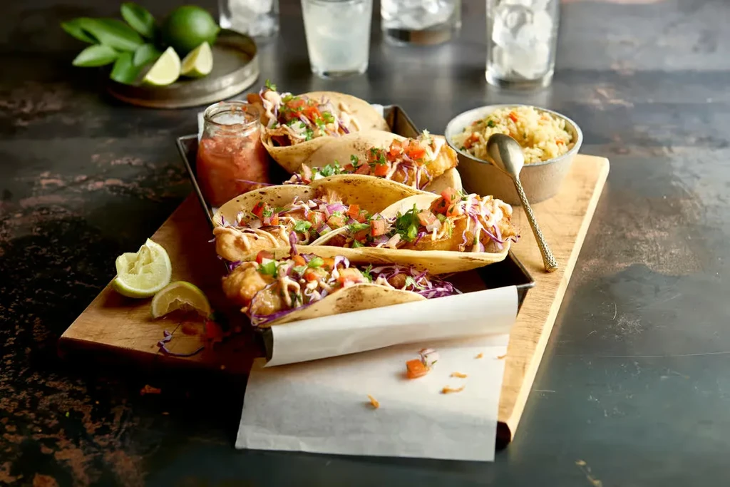 Four fish tacos with slaw, salsa, rice, and limes.