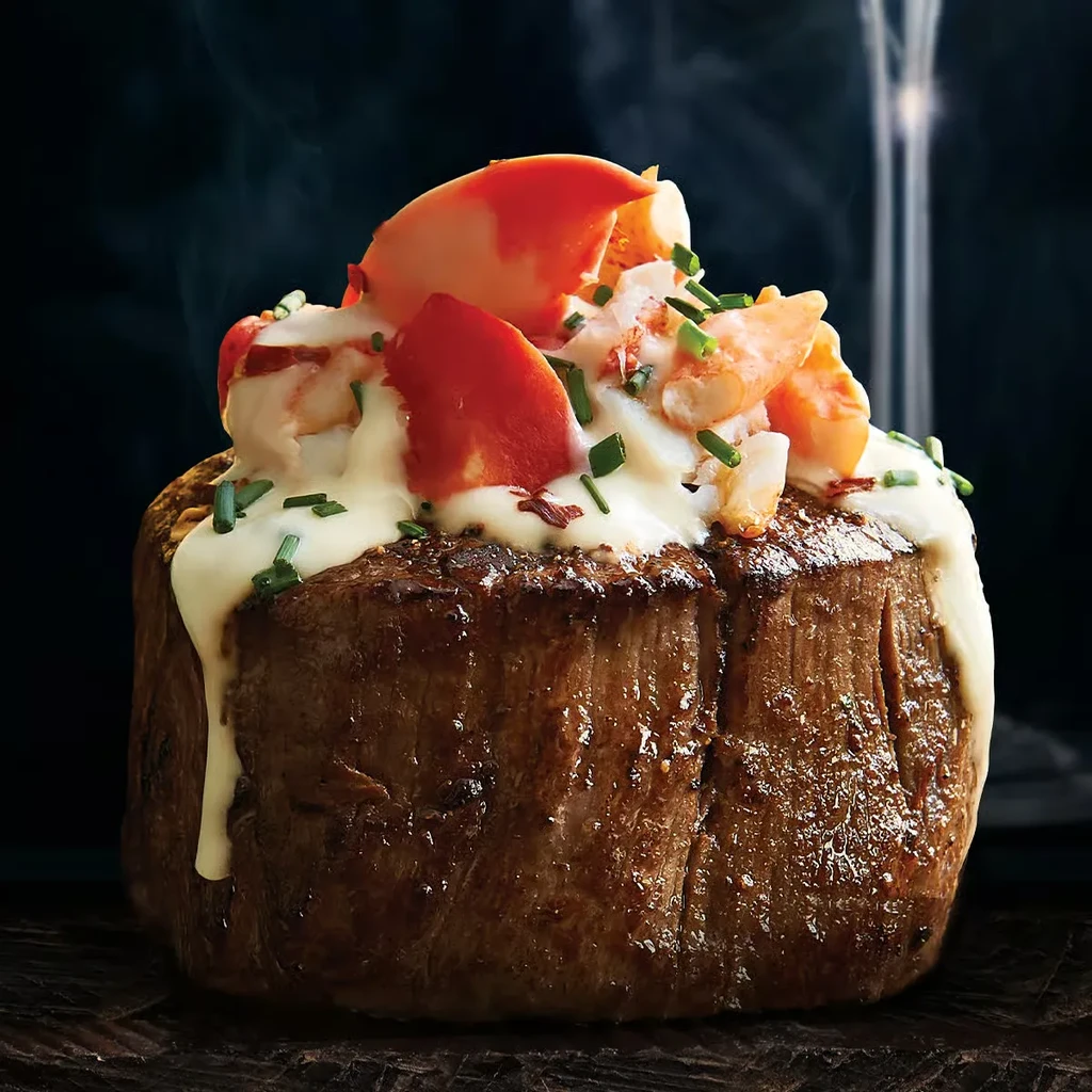 Steaming seared steak topped with creamy sauce, lobster, and chives.