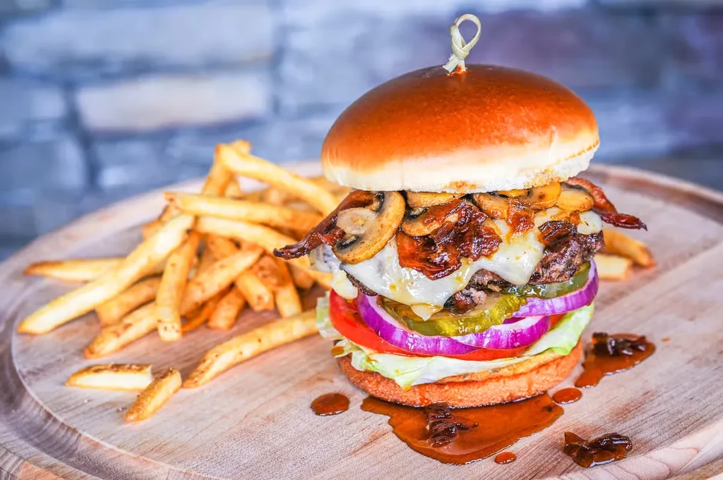 Large gourmet burger and golden fries on a wooden board.