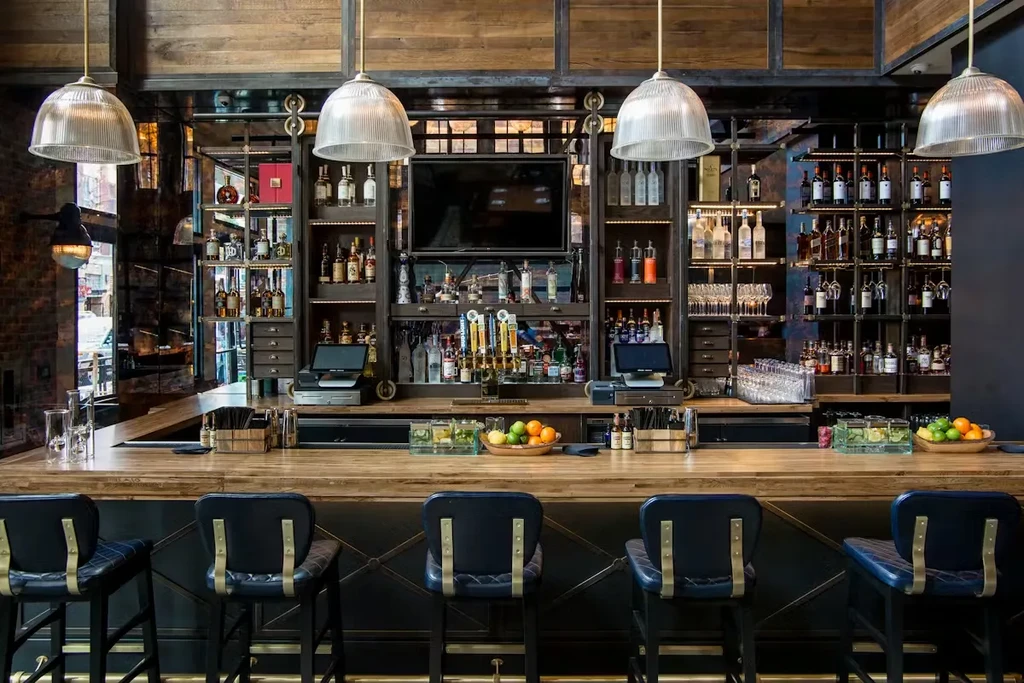 Bright, empty bar with wood counter, blue stools, and liquor bottles.