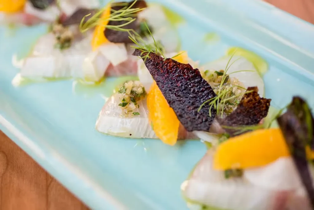 Close-up of white fish ceviche with orange, crispy chips, green herbs.