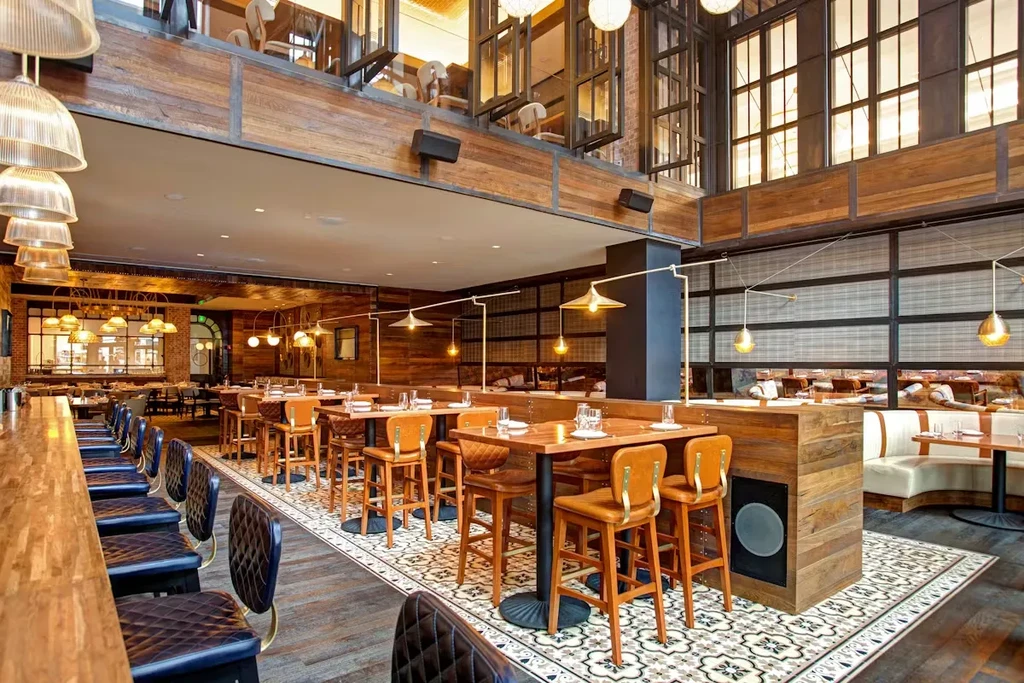 Stylish modern restaurant interior with bar, dining tables, and exposed wooden beams.