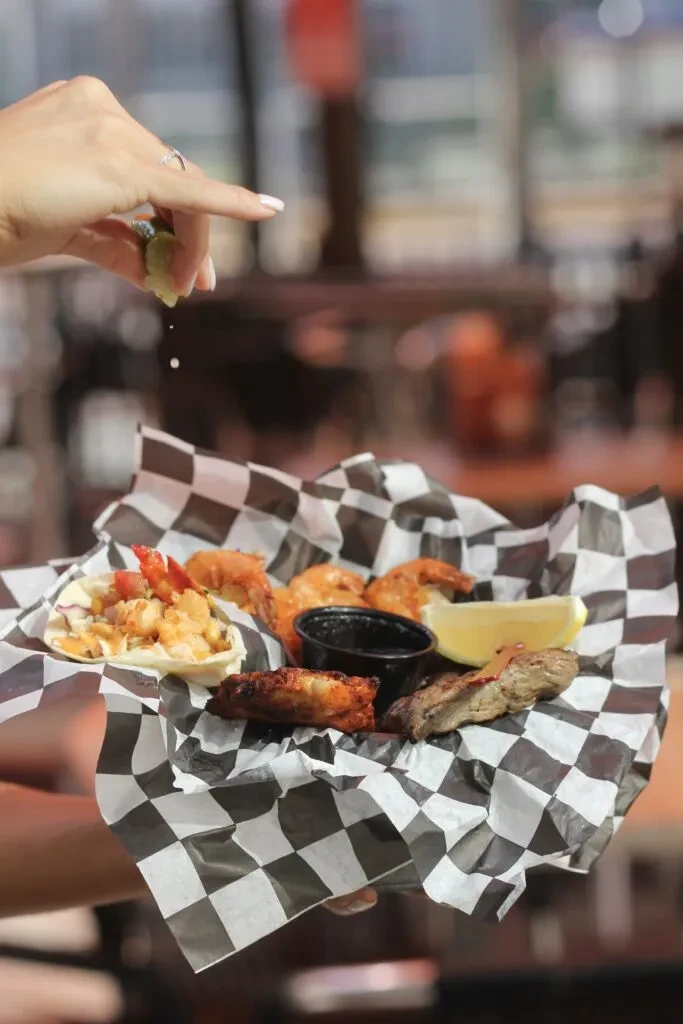 Assorted appetizers in a checkered basket with a hand squeezing lime.