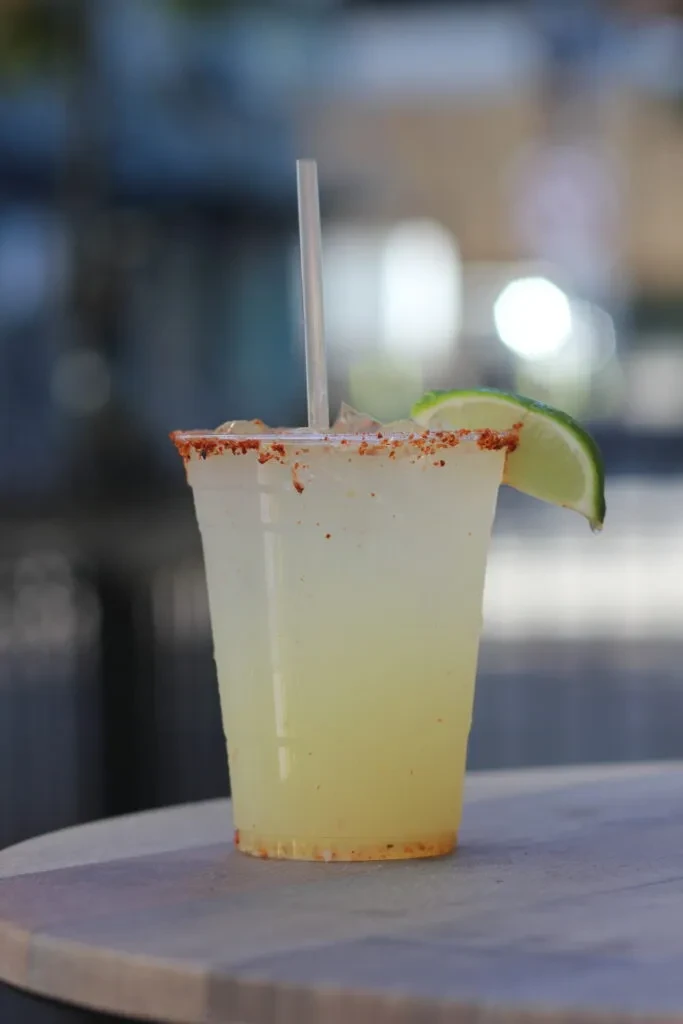 Clear plastic cup with iced yellow drink, chili rim, lime wedge.