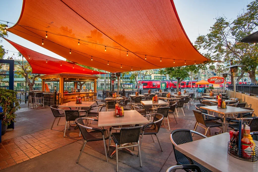 Empty outdoor restaurant patio with orange shade sails and string lights.