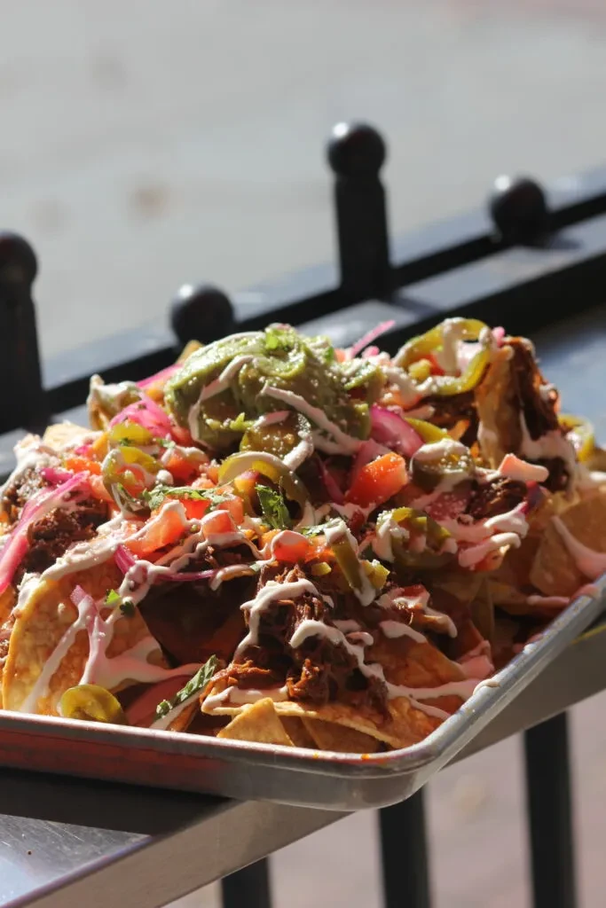 Large nachos with meat, guacamole, and many toppings on a metal tray.