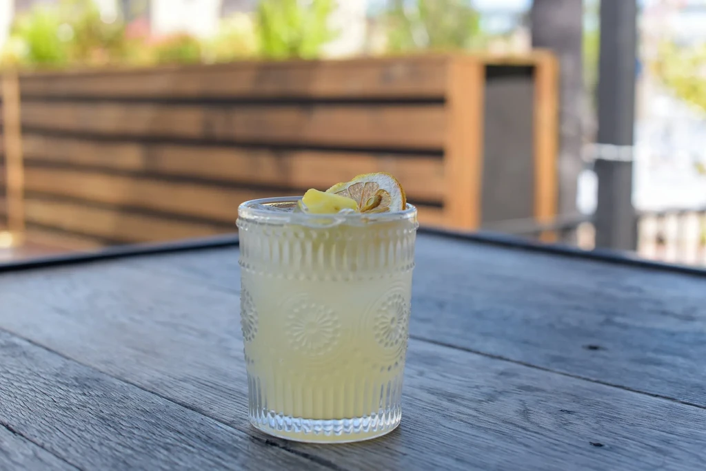 Garnished pale drink in ornate glass on a weathered wooden table outdoors.