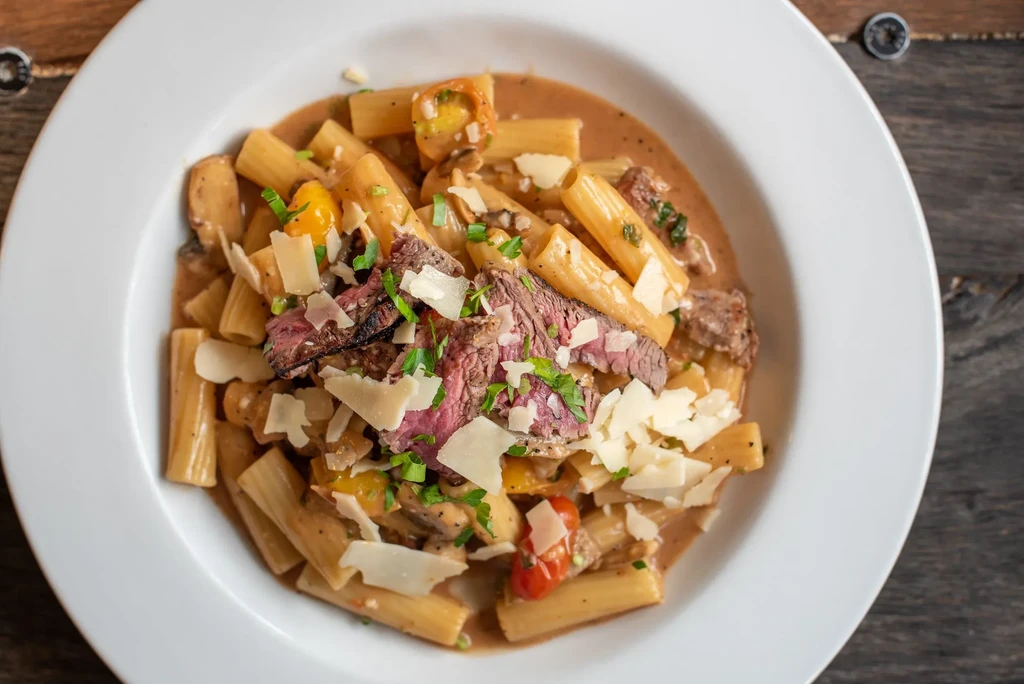 Rigatoni pasta with grilled steak, creamy sauce, Parmesan, and herbs.