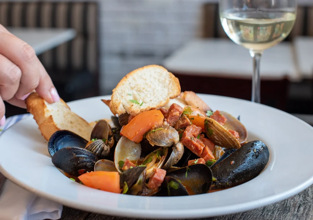 Hand holding bread in seafood stew with mussels and chorizo.