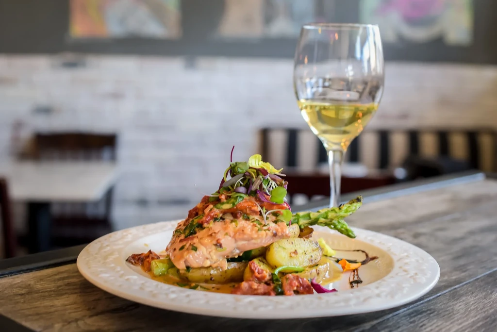 Plated salmon, roasted potatoes, asparagus, and white wine in a restaurant.