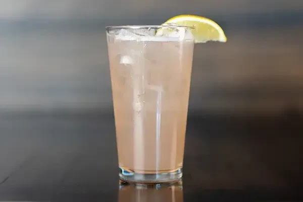 Cold pinkish-brown drink with ice and lemon/lime wedge in glass.