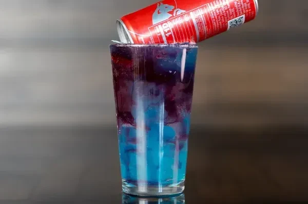 Layered blue and red-purple drink with inverted red energy can on rim.