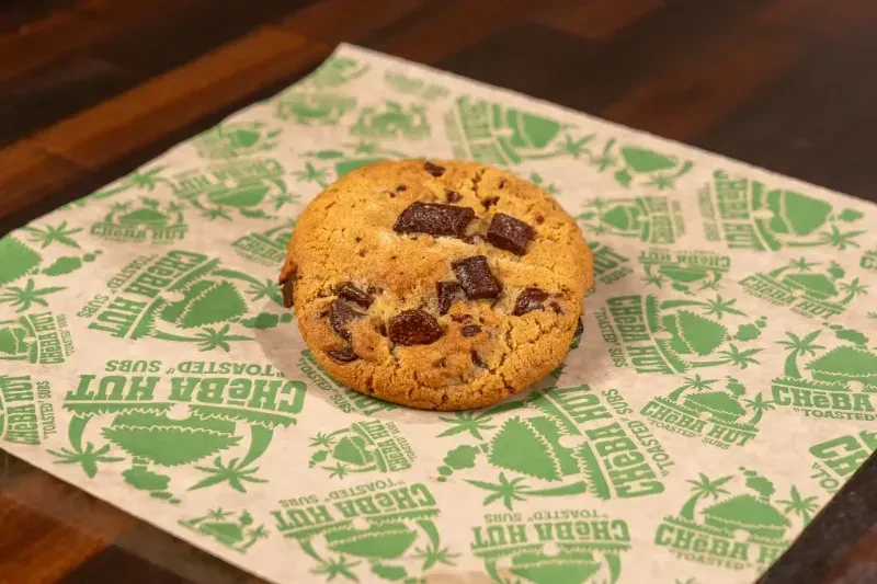Golden chocolate chip cookie on Cheba Hut cannabis-themed wax paper.