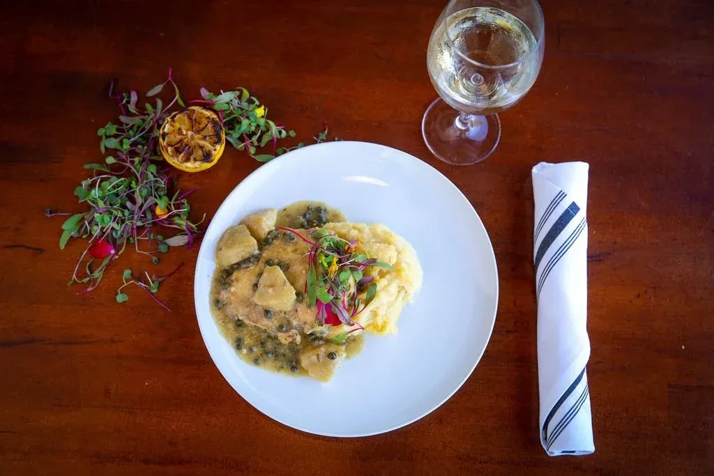 Plated meal: Protein in sauce, mashed potatoes, lemon, microgreens, white wine.