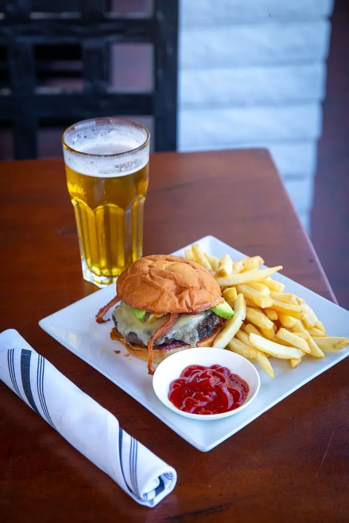 Gourmet burger, fries, ketchup, and beer on a wooden table.