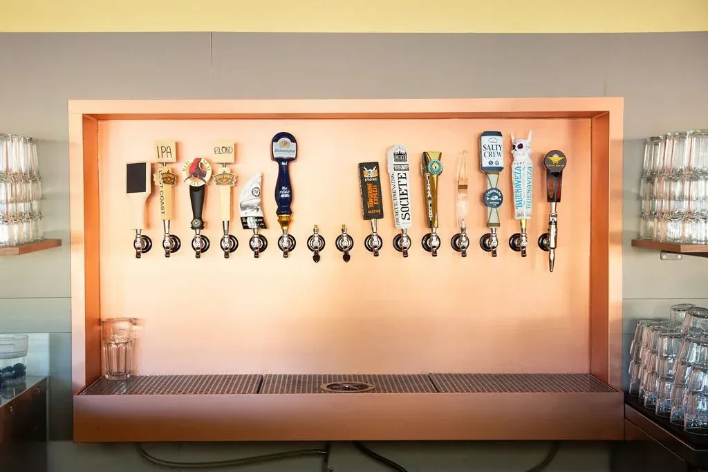 Sixteen beer taps on a copper panel with an empty pint glass.