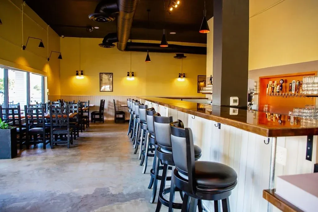 Modern restaurant interior with dining tables and a long bar with beer taps.