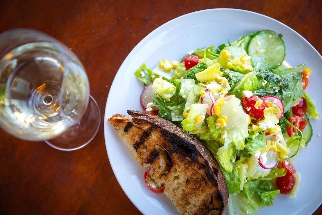 Overhead view of a fresh salad, grilled toast, and white wine.