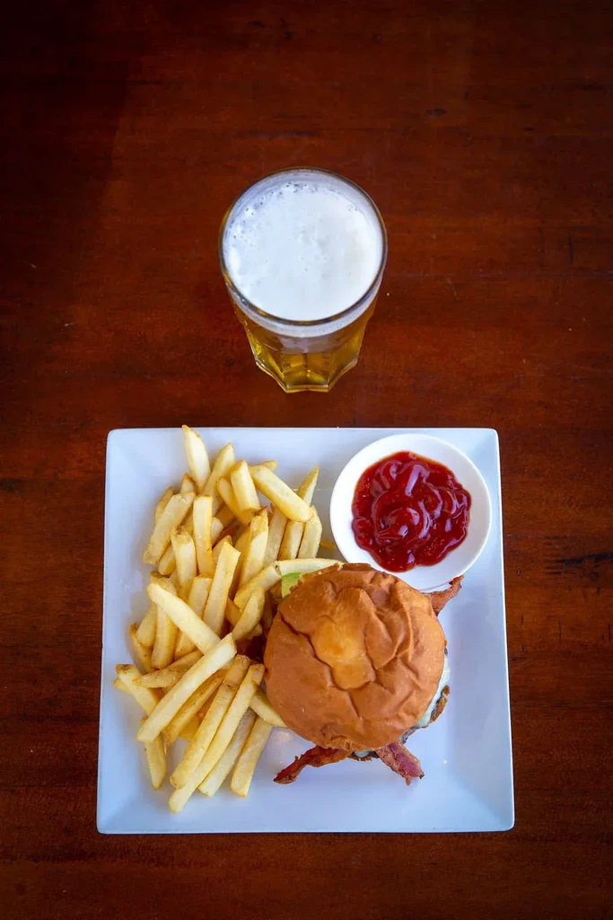 Overhead shot of burger, fries, ketchup, and beer on wooden table.