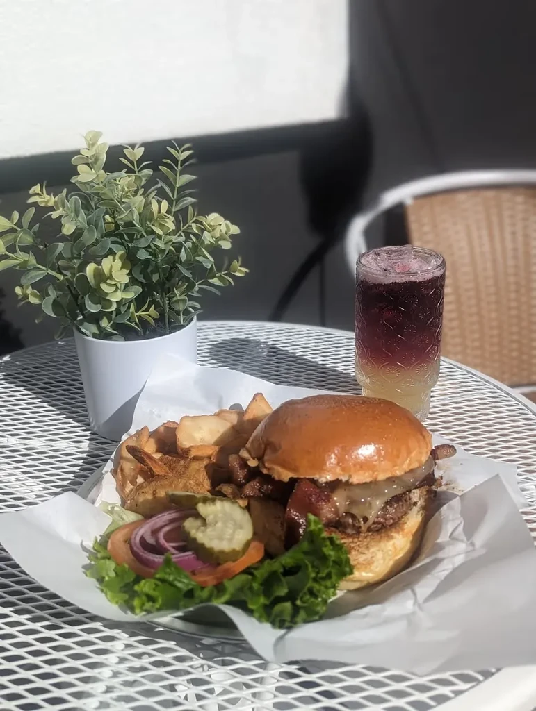 Gourmet bacon cheeseburger, rustic fries, and a layered drink on an outdoor table.