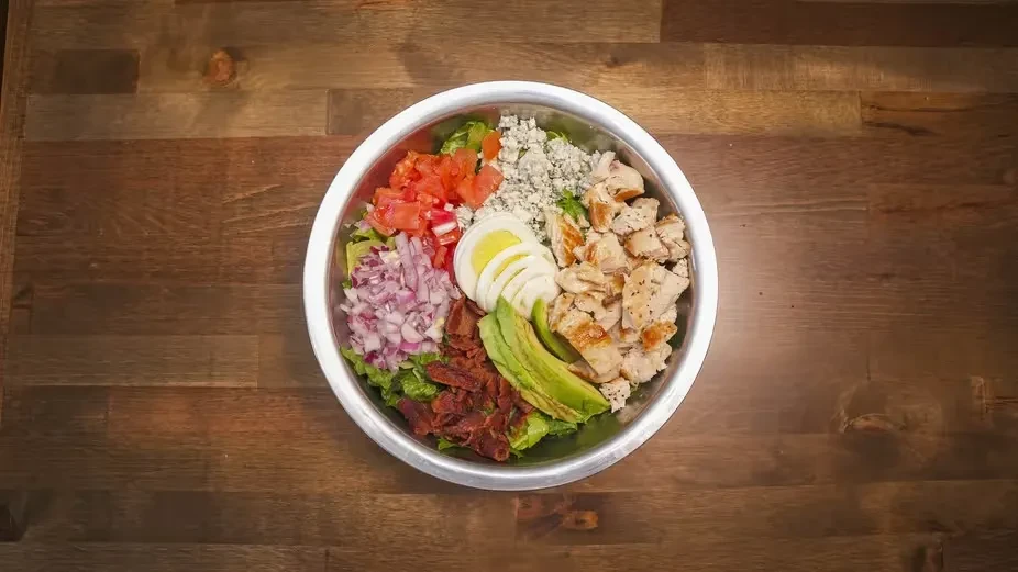 Cobb salad, neatly arranged in a silver bowl on a wooden table.
