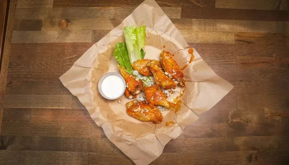 Top-down view of sauced chicken wings, blue cheese, dip, and lettuce.