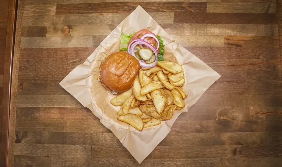 Top-down deconstructed hamburger, potato wedges, and fresh toppings on wood.