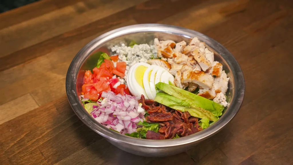Cobb salad with chicken, avocado, and egg in a metal bowl.