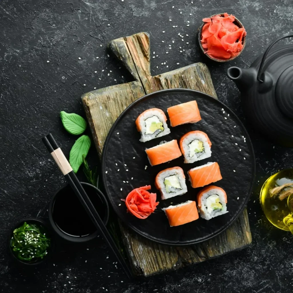 Top-down of eight salmon sushi rolls, pickled ginger, on dark plate.