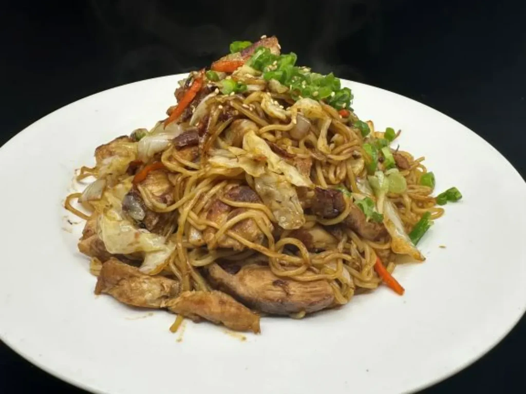 Steaming stir-fried chicken noodles with vegetables and sesame seeds.
