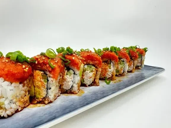 Eight sushi rolls with orange topping, sesame, and green scallions on dark plate.