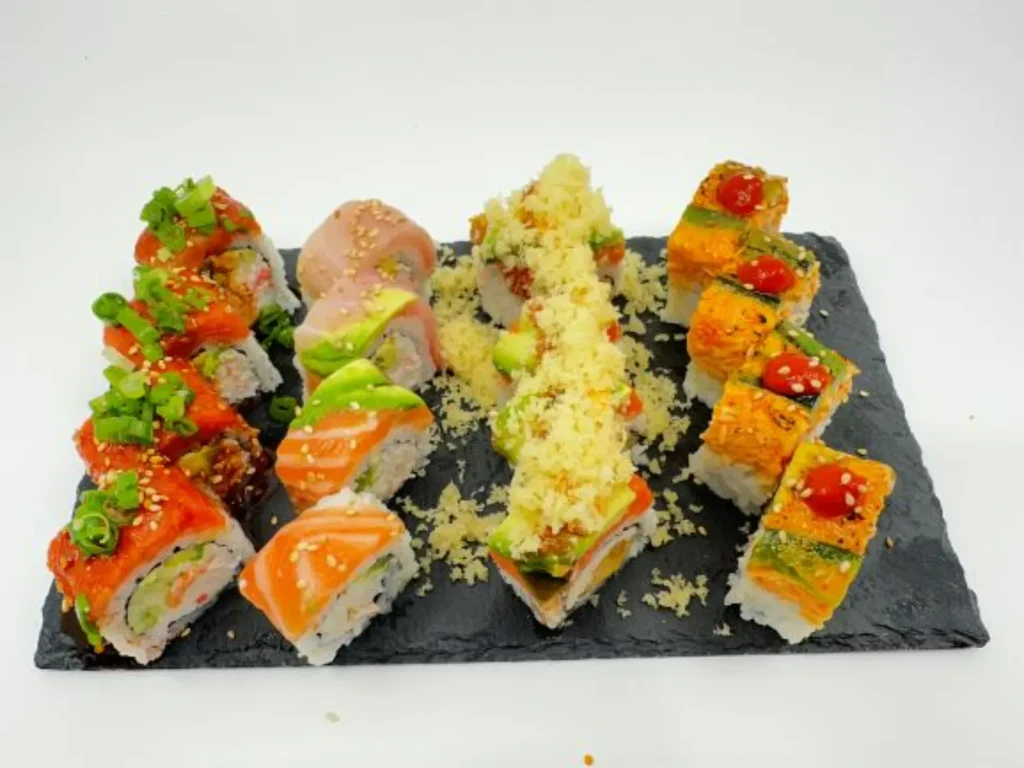 Vibrant assortment of sushi rolls on a dark slate plate.