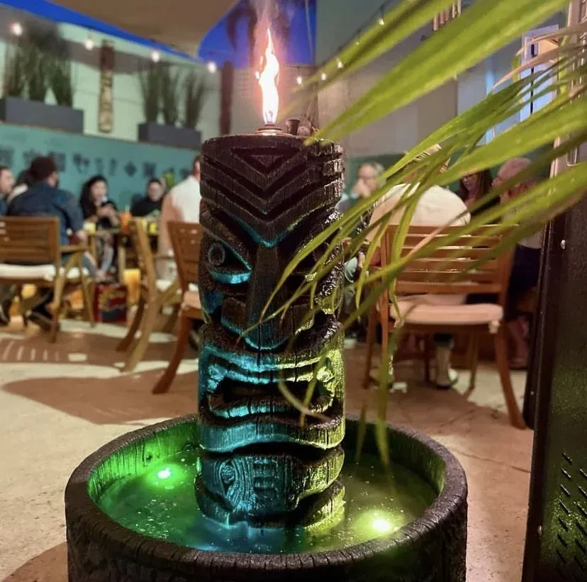 Carved tiki fountain with flame and green light on an outdoor patio.