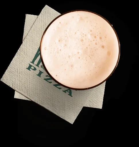 Top-down view of foamy drink in glass on 'M & PIZZA' napkins.