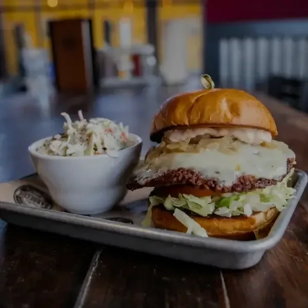 Toasted brioche burger, melted cheese, and creamy coleslaw on a tray.