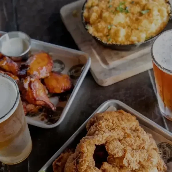 Baked dish, glazed chicken, fried food, and two beers on a dark table.
