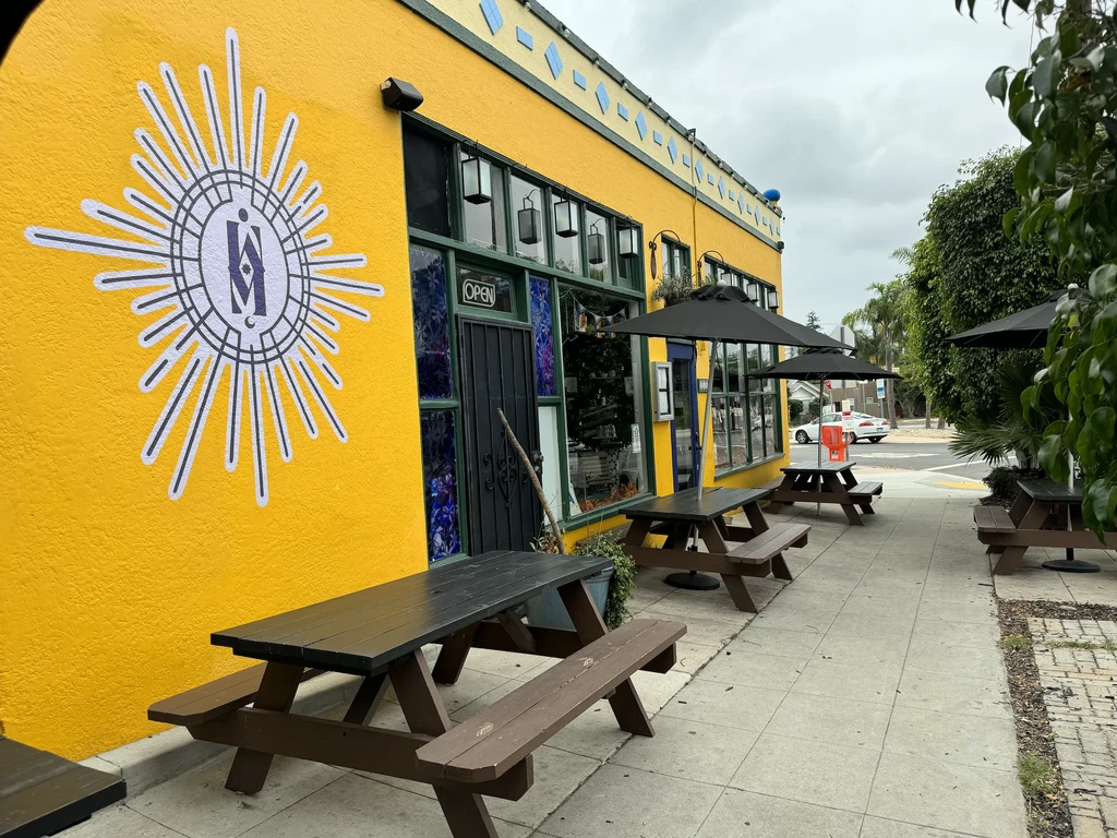 Yellow building with sunburst mural, 'OPEN' sign, and patio tables.