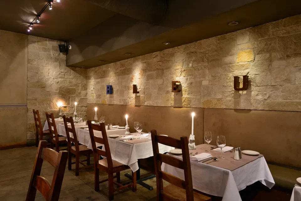 Restaurant dining space: stone wall, set tables, illuminated by spotlights.
