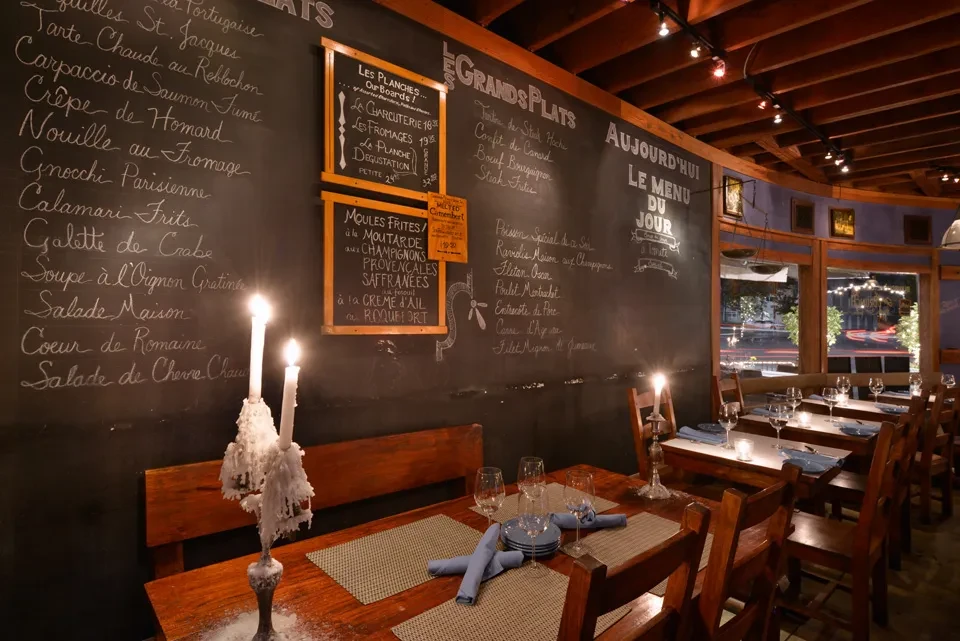 Rustic restaurant with set tables, lit candles, and chalk wall menus.