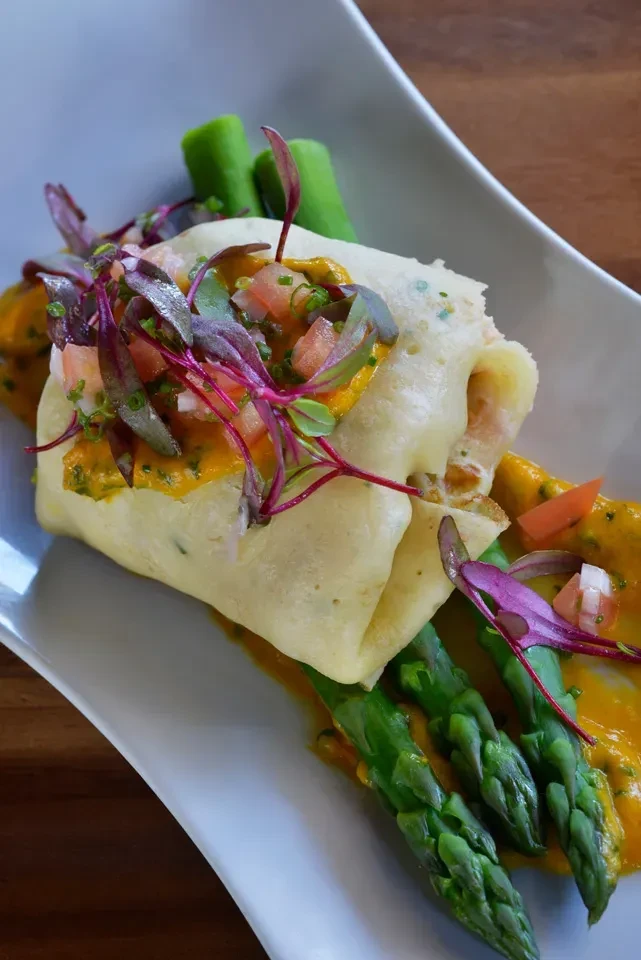 Rolled item on orange sauce, asparagus, tomato, and microgreens.