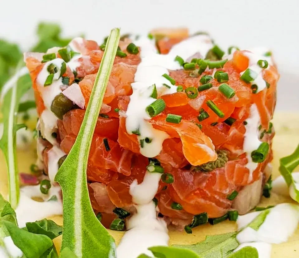 Finely diced salmon tartare topped with sauce, chives, and green leaves.