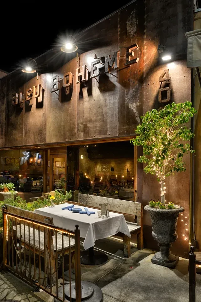 Illuminated BLEU BOHEME restaurant sign and outdoor patio at night.
