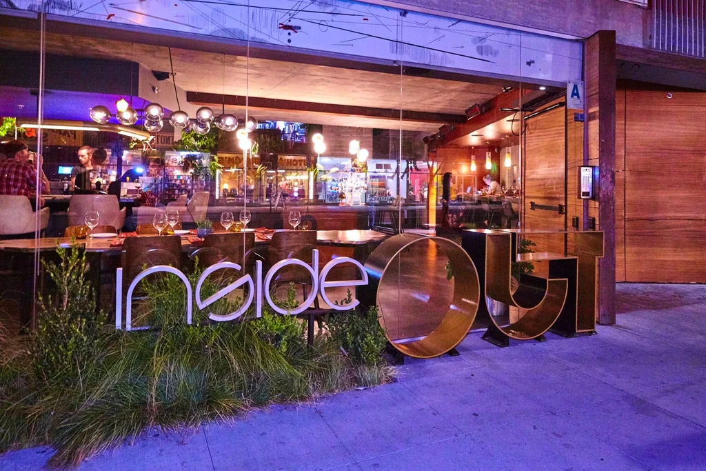 Modern restaurant 'Inside Out' at night, name split across planter and sidewalk.