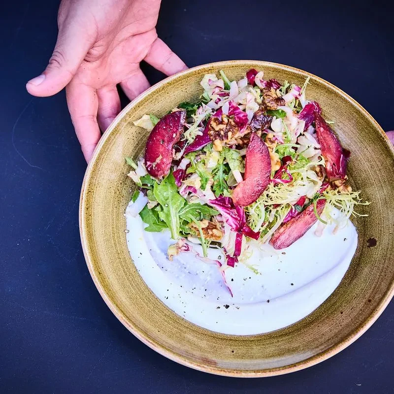 Overhead salad with greens, radicchio, walnuts, plum slices, held by hand.