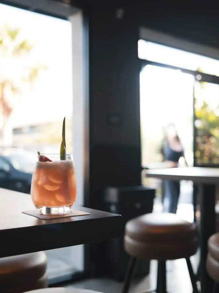 Frothy peach cocktail with green leaf, red fruit on a wooden table.