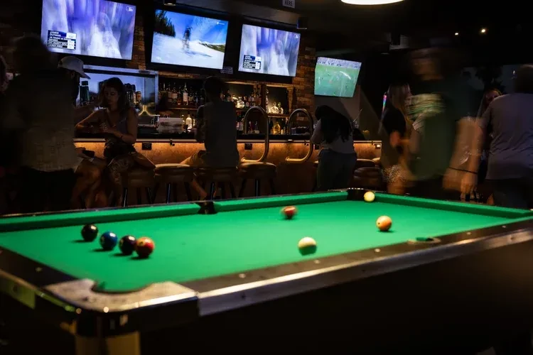 Pool table in a dimly lit, lively bar with blurred patrons.