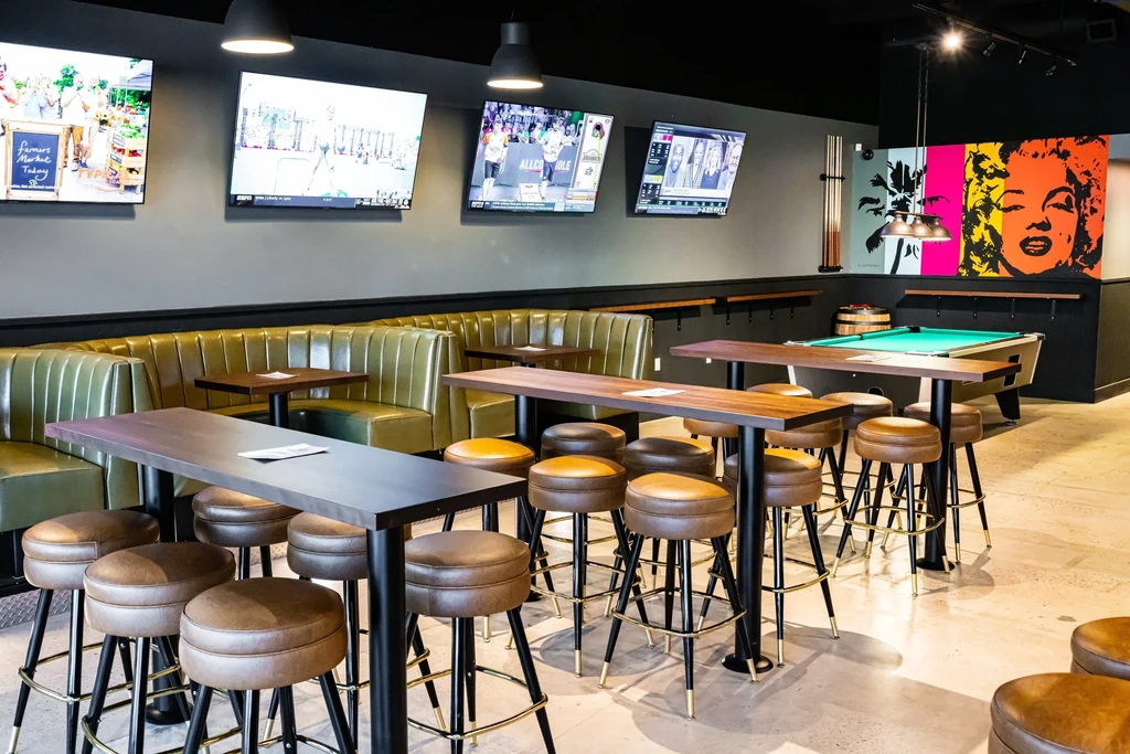 Modern restaurant interior featuring booths, high-tops, TVs, and a pool table.